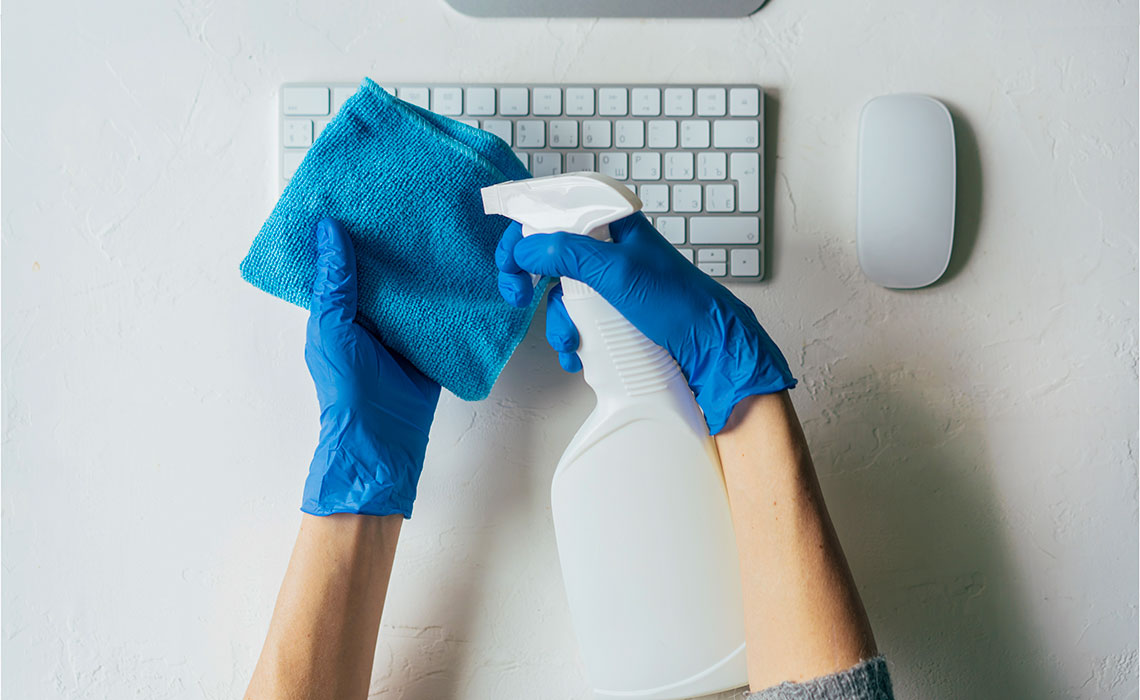 Gloved hand uses spray cleaner to disinfect office desk